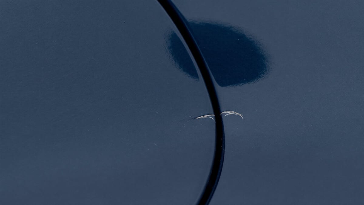 A small scratch in dark car paint beside a panel gap
