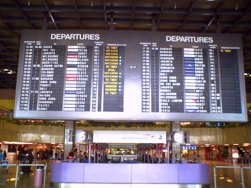 An airport departure board and a plane at the gate